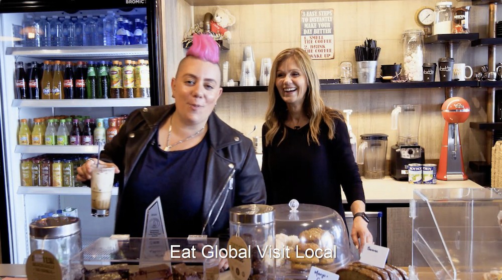 Woman with pink hair in cafe laughing and pretty woman in background also laughing